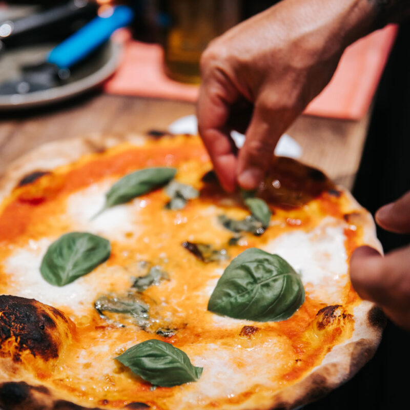 Person garniert frisch gebackene Pizza mit Basilikum